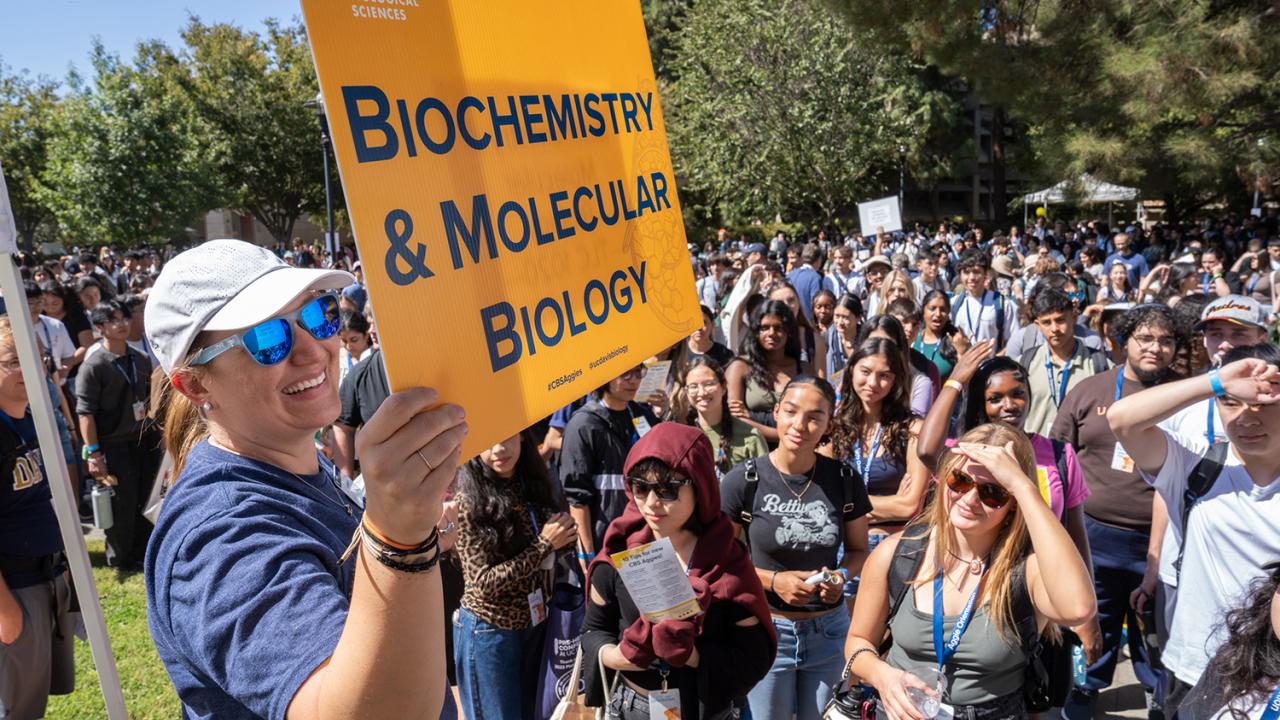 Orientation leader holds a “Biochemistry & Molecular Biology” sign as a large group of new UC Davis students gather outside.