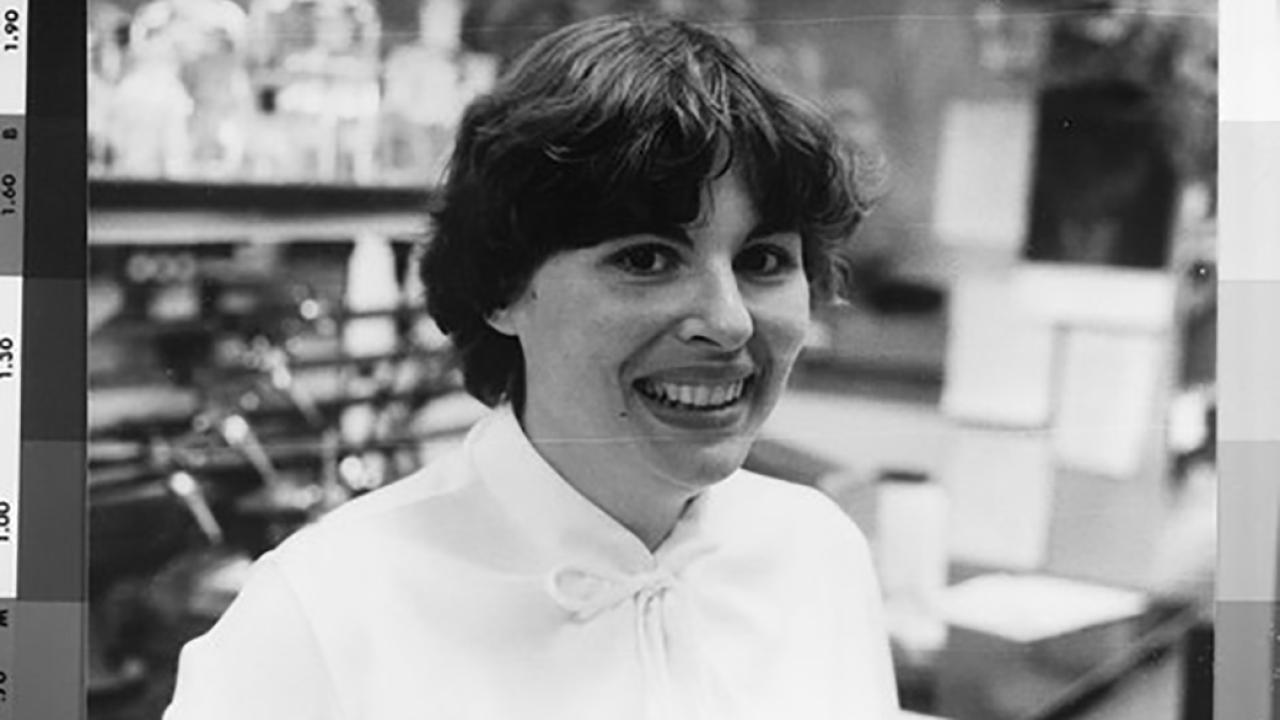 Black-and-white photo of Marilynn Etzler smiling in a lab, wearing a light blouse with a bow at the collar.